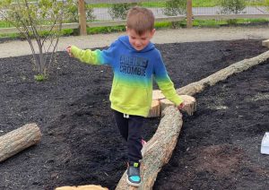young boy walking on log in play garden